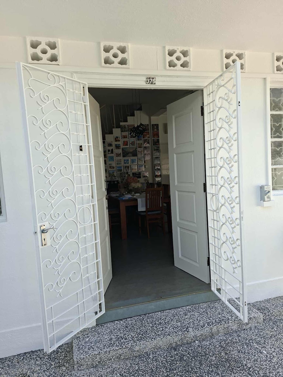 Double door entry with both leaves freshly painted white and ornate white gates open