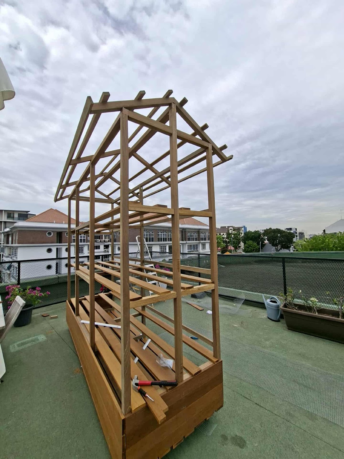 Custom timber aviary frame under construction on a roof terrace, hammer resting on a beam